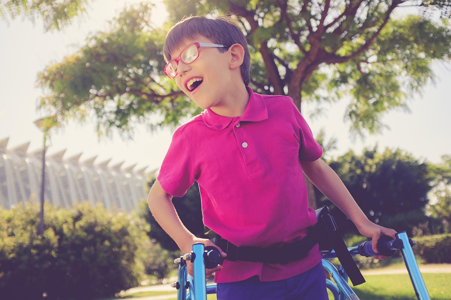 Nine year boy enjoying a walk in a sunny park using walking frame